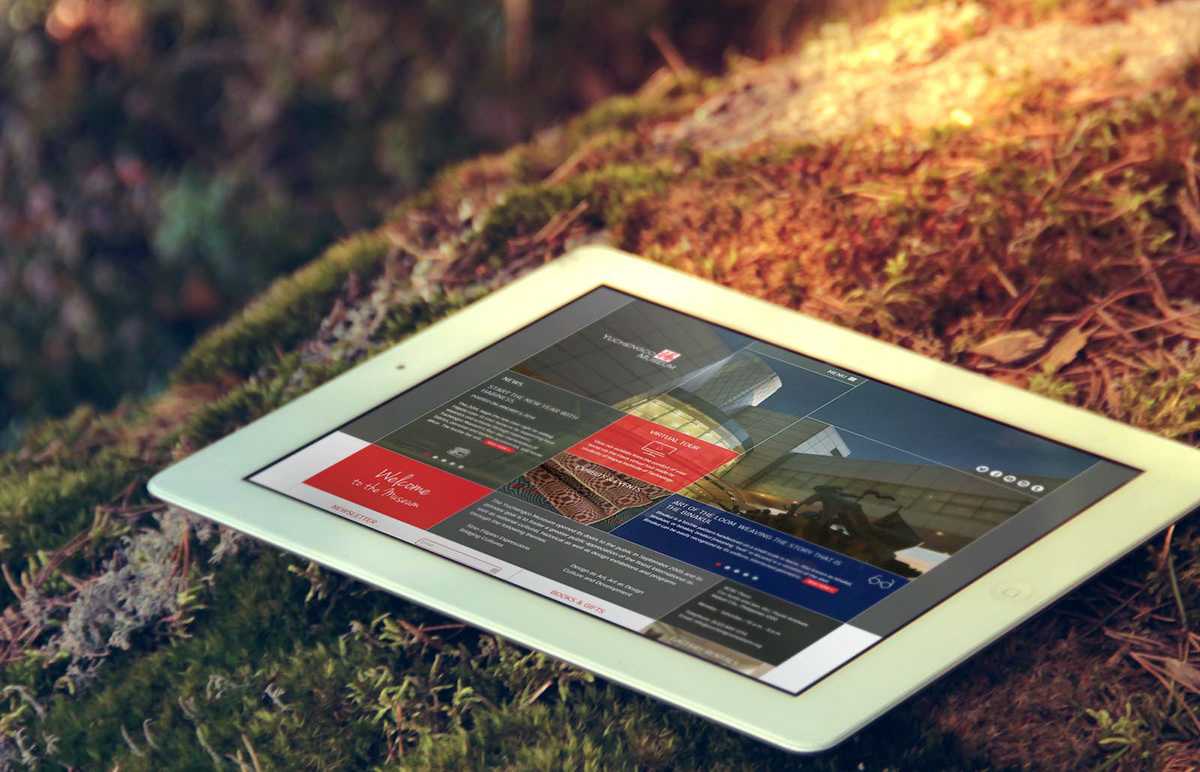 The Yuchengco Museum homepage shown on a tablet resting on moss in a forest, with the tiled layout and the Welcome to the Museum panel